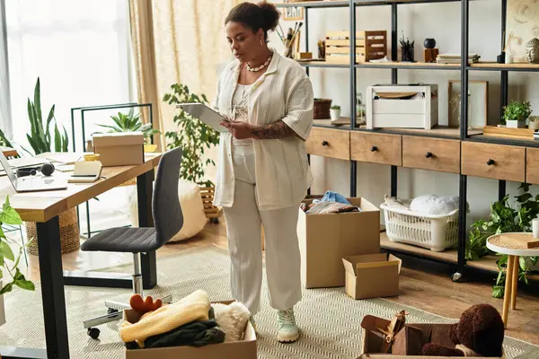 In a cozy crafting workshop, a beautiful woman examines her creative notes among boxes of supplies. — Stock Photo