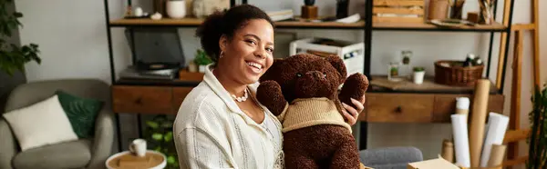 A smiling woman holds a teddy bear, surrounded by cozy workshop elements. — Stock Photo