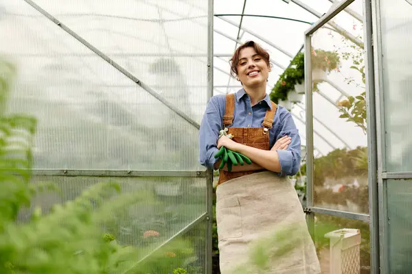 Dans une serre ensoleillée, une jeune femme sourit tout en tendant vers des plantes vibrantes. — Photo de stock