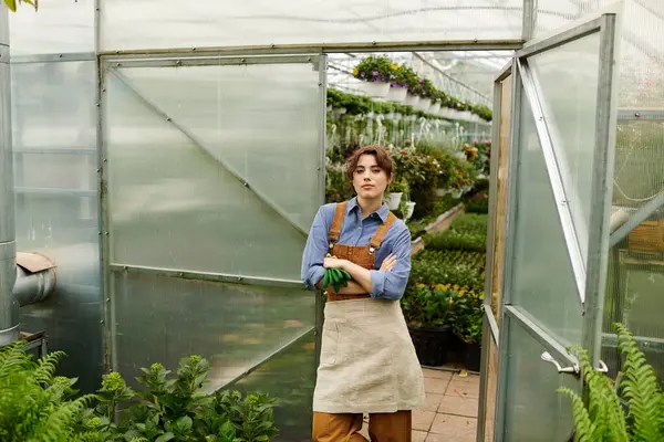 A young woman stands proudly in a greenhouse surrounded by flourishing plants, radiating bliss. — Stock Photo