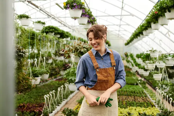 Uma jovem mulher alegremente nutre suas plantas em crescimento em uma estufa exuberante repleta de vegetação fresca. — Fotografia de Stock