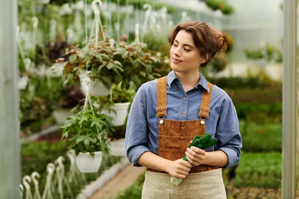 A young woman with a green thumb enjoys nurturing various plants in a vibrant greenhouse. — Stock Photo