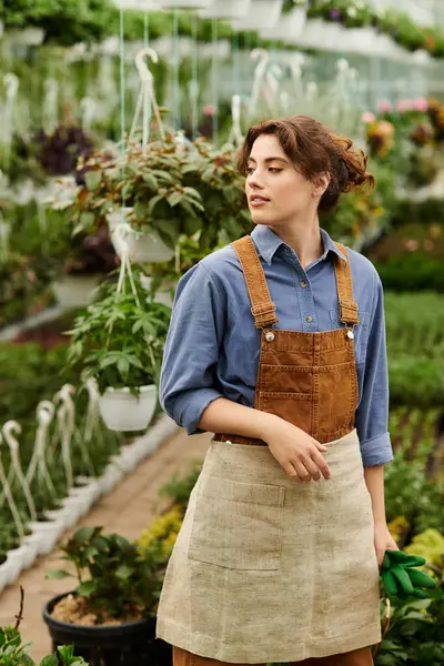 Mujer joven que tiende a plantas prósperas en un invernadero brillante lleno de exuberante vegetación. - foto de stock