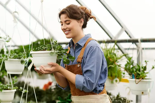 A young woman joyfully nurtures potted plants in a bright greenhouse, showing her green thumb. — Stock Photo