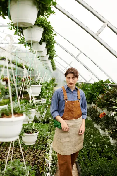 A young woman skillfully tends to her potted plants in a thriving greenhouse, basking in bliss. — Stock Photo
