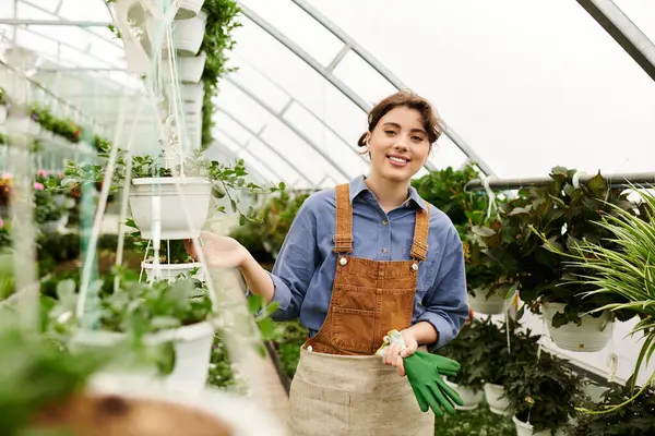 In a sunlit greenhouse, a young woman joyfully tends to lush green plants with care and passion. — Stock Photo