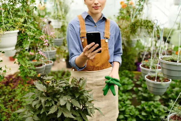 A young woman enjoys nurturing her plants in a sunlit greenhouse filled with greenery. — Stock Photo