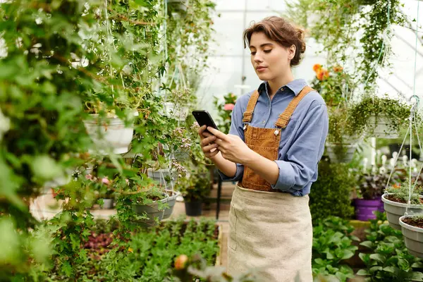 A young woman tends to her plants in a greenhouse, thoughtfully managing her garden space. — Stock Photo