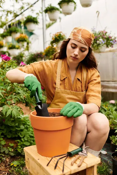 A blissful gardener in a headscarf plants seeds in a terracotta pot within a sunny greenhouse. — Stock Photo