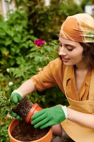 Une jeune femme avec un foulard s'occupe amoureusement de ses plantes dans une serre vibrante. — Photo de stock