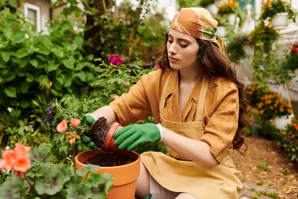Uma jovem mulher em um lenço de cabeça cuida de suas plantas, alimentando-as com cuidado em uma estufa animada. — Fotografia de Stock