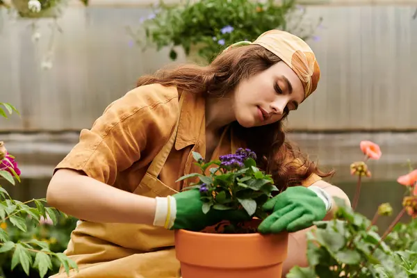 En un alegre invernadero, una joven en un pañuelo nutre sus plantas con cuidado. - foto de stock