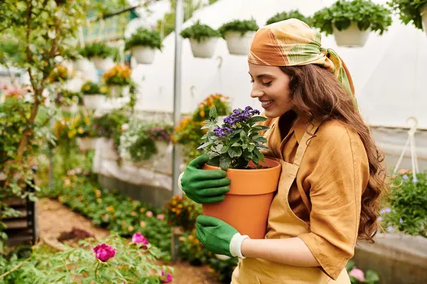 A passionate gardener smiles while holding a potted flower in a lush greenhouse. — Stock Photo
