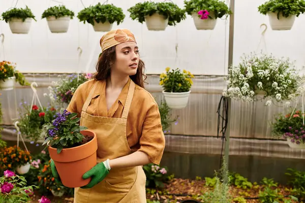 A young woman in a headscarf tends to colorful flowers in a thriving greenhouse. — Stock Photo