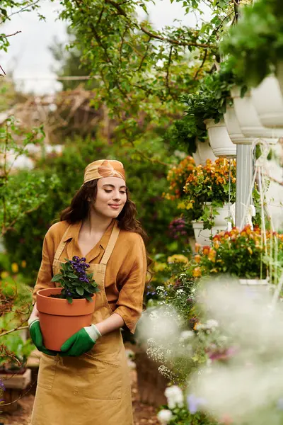 A young woman in a headscarf nurtures plants in a lively greenhouse, surrounded by colorful flowers. — Stock Photo