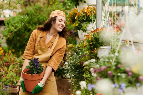 A young woman in a headscarf smiles joyfully while tending to plants in a lush greenhouse. — Stock Photo