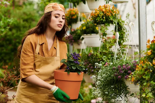 Young woman in a headscarf nurtures potted plants in a lively greenhouse, showcasing her passion. — Stock Photo