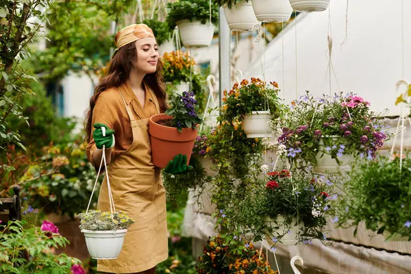 Счастливая молодая женщина в платке и фартуке имеет тенденцию цвести в оранжерее. — стоковое фото