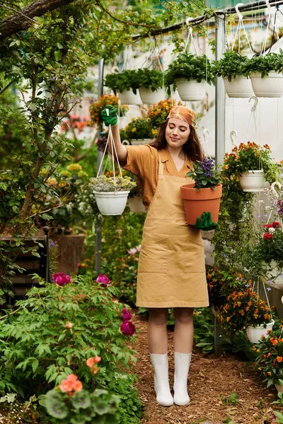 Brightly dressed woman holds potted plants, nurturing life in a beautiful greenhouse. — Stock Photo