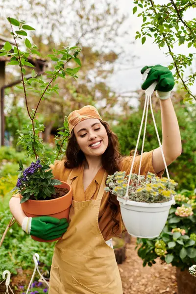 A cheerful young woman in a headscarf nurtures potted plants while enjoying her greenhouse oasis. — Stock Photo