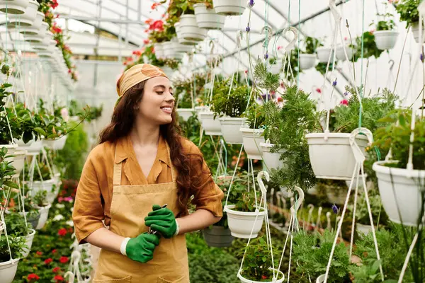 In a serene greenhouse, a young woman in a headscarf lovingly grows various plants with joy. — Stock Photo