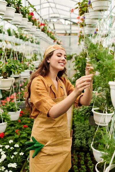 A joyful young woman in a headscarf tends to her flourishing plants in a sunny greenhouse. — Stock Photo