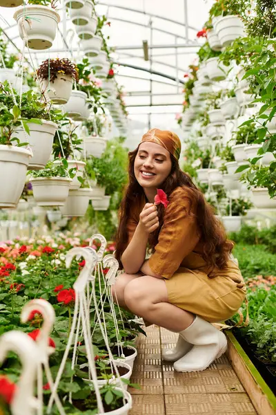 Uma mulher feliz em um lenço de cabeça tende a plantas vibrantes, abraçando a beleza da natureza em uma estufa. — Fotografia de Stock