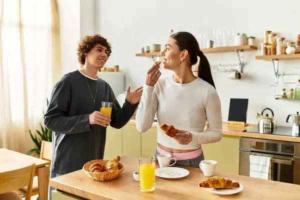 A couple shares laughter and delicious croissants while sipping fresh juice in their warm home. — Stock Photo