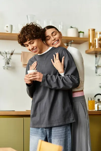 Em uma cozinha acolhedora, uma mulher abraça um homem sorridente por trás, ambos se divertindo. — Fotografia de Stock