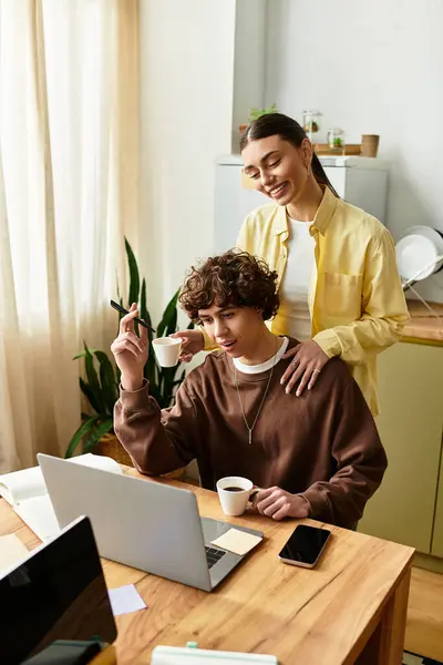 A man focuses on his laptop while a woman lovingly stands behind him, enjoying their time together. — Stock Photo