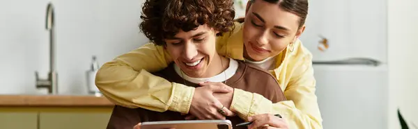 Loving couple embraces in their warm home, sharing laughter and joy while using a tablet together. — Stock Photo