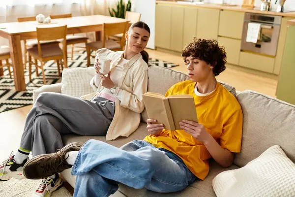 A couple relaxes on the couch, sharing a book and enjoying a beverage in their cozy home. — Stock Photo