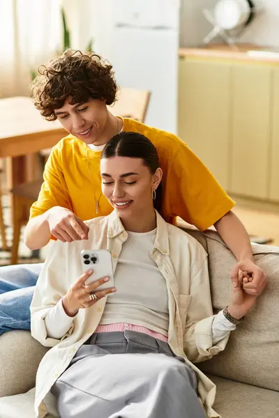 Una alegre pareja disfruta del tiempo de calidad juntos, mirando un teléfono mientras están abrazados en el sofá. - foto de stock