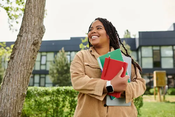 Un insegnante universitario sorride calorosamente, stringendo vivaci quaderni in una giornata soleggiata del campus. — Foto stock
