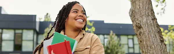 Donna sorridente abbraccia il calore della giornata, portando vivaci quaderni in un campus universitario. — Foto stock