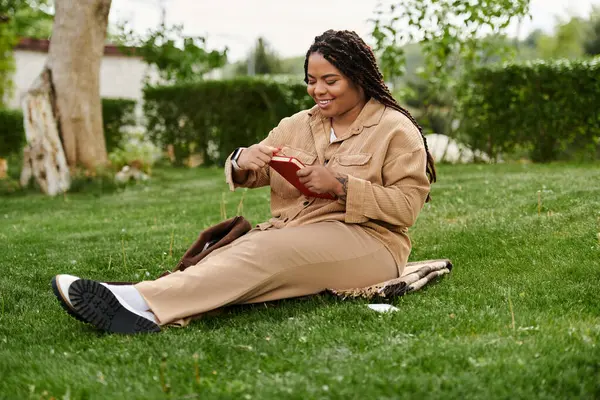 Une professeure d'université se détend sur l'herbe, profondément engagée dans son livre dans la tranquillité des natures. — Photo de stock