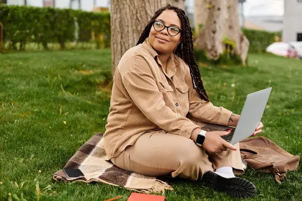 A dedicated university teacher sits on a blanket in a lush green park, engaged with her laptop. — Stock Photo