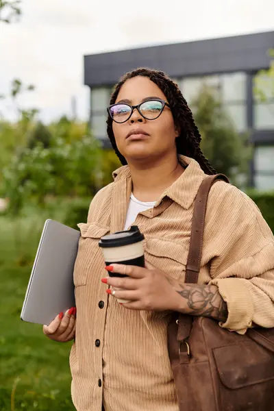 A university teacher outdoors, confidently holding a laptop and coffee, reflecting on ideas. — Stock Photo