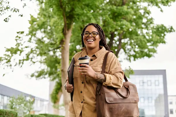Un professeur souriant se promène sur le campus avec café et documents, profitant de la journée. — Photo de stock