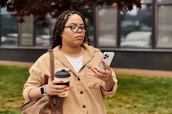 Una profesora universitaria comprueba su teléfono con café en un ambiente relajado al aire libre. - foto de stock