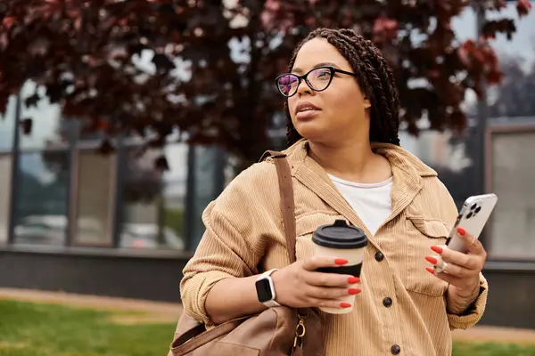 A woman pauses with a coffee in hand, looking thoughtfully around her university campus during fall. — Stock Photo