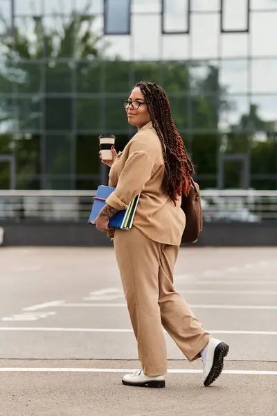A university teacher strolls across the campus with books and a coffee cup, enjoying the day. — Stock Photo