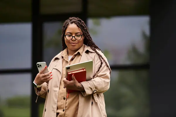 Una profesora universitaria está afuera, sosteniendo una tableta y un teléfono, lista para su próxima clase. - foto de stock