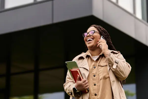 Una donna parla felicemente al telefono mentre tiene il tablet fuori da un edificio moderno. — Foto stock