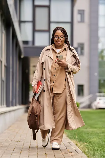 Femme éducatrice se promène dans les terrains universitaires, engagée avec son smartphone et portant des livres. — Photo de stock
