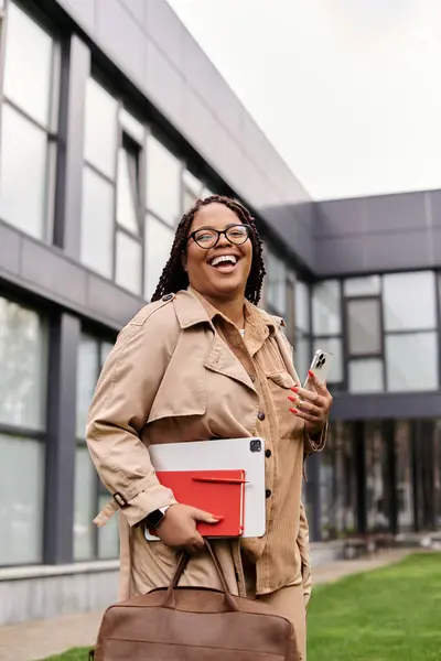A happy university teacher smiles outdoors, holding a notebook under clear skies. — Stock Photo