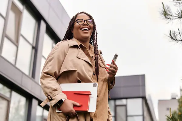 Happy woman with a tablet and phone smiles while walking outside university buildings. — Stock Photo