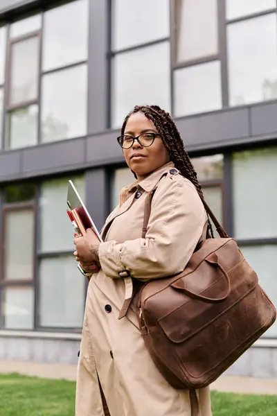 Une femme confiante se tient devant un bâtiment universitaire, tenant des livres et une tablette. — Photo de stock