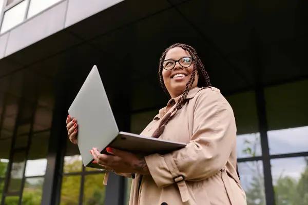 Une femme sourit devant une université, utilisant son ordinateur portable pour se connecter avec des étudiants. — Photo de stock
