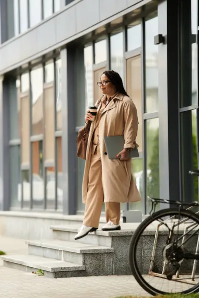 A university teacher stands at the entrance, sipping coffee while carrying a laptop. — Stock Photo